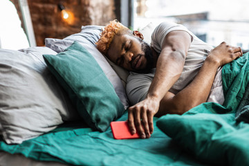 Fototapeta premium Nice sleepy man taking his mobile phone