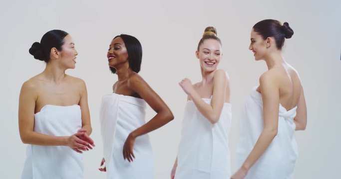 Slow motion of beautiful young smiling women of different ethnicities with perfect firm and slim body in white bathing towels dancing and having fun isolated on white background.