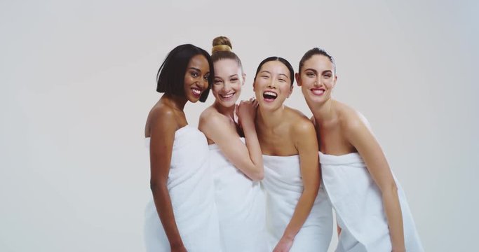 Slow motion of beautiful young women of different ethnicities with perfect firm and slim body in white bathing towels having fun and laughing in camera isolated on white background. 