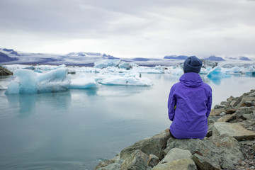 A young woman admires the blue ice in the ice lagoon of Iceland. Tourist with a red backpack