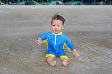 Happy of Asian baby boy in swimming suit sitting on the sand beach.