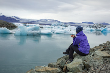 A young woman admires the blue ice in the ice lagoon of Iceland. Tourist with a red backpack