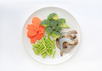 Raw Shrimp with chopped vegetable on white plate against white background.