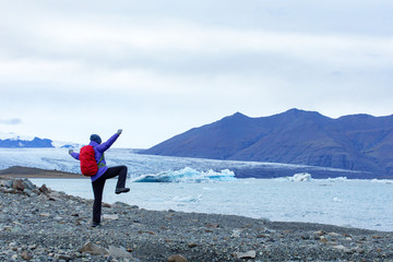 Obraz premium A young woman admires the blue ice in the ice lagoon of Iceland. Tourist with a red backpack