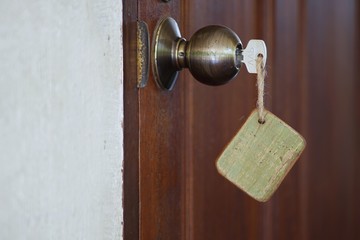 Home key with wooden blank house keychain in keyhole, property concept