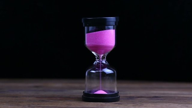 Hourglass on a Black Background, Sand Falls Inside.