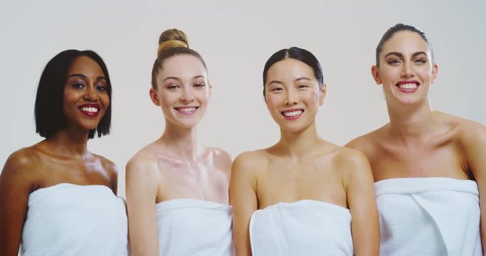 Slow motion of beautiful young women of different ethnicities with perfect firm and slim body in white bathing towels looking and smiling in camera isolated on white background. 