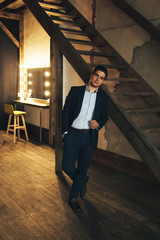 dark-haired man in a jacket stands clinging on the stairs