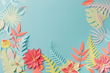Colourful handmade tropical paper flowers and leaves on blue pastel background with copyspace in the middle, summer spring flower concept, papercraft origami idea