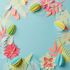 Colourful handmade tropical paper flowers and leggs on blue pastel background with copyspace, seasonal easter wreath, summer spring flower, papercraft origami idea