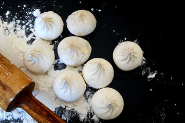 raw homemade handmade forcemeat big dumplings, rolling pin and white wheat flour on the kitchen black table