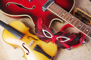 Electric guitar, violin, carnival mask, tambourine on a wooden background.