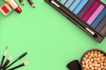 Top, up view of professional cosmetics, makeup background. Brushes, eye shadows, eyebrow pencils, powder, bronzing balls, mascara, red lipstick. Tools isolated on green. Concept of get ready for party