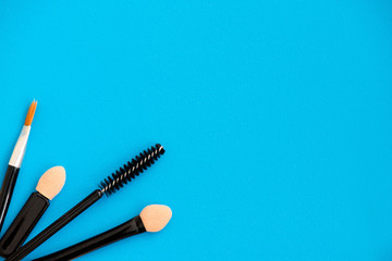 Top, up view of professional cosmetics, makeup background. Brushes, eye shadows, eyebrow pencils, powder, bronzing balls, mascara, red lipstick. Tools isolated on blue. Concept of get ready for party