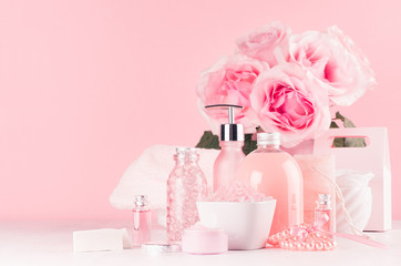 Fototapeta na wymiar Elegant pink skin and body care products - cream, rose oil, liquid soap, salt, cotton towel and box - cosmetic accessories, romantic flowers on white wood table.