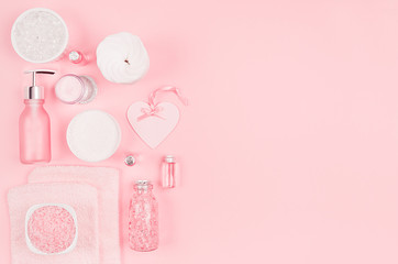 Cosmetic products and accessories in pink color - cream, bath salt, essential oil, soap, towel, bottles, heart, bowl on pink background, top view.