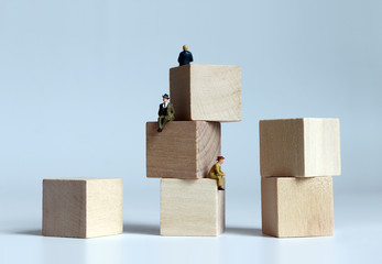 Miniature people sitting on stack of wooden blocks.