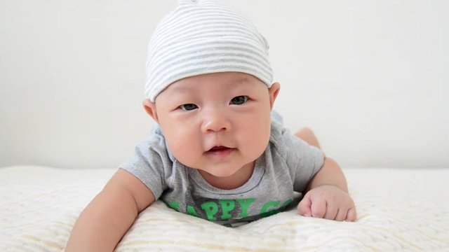 cute little asian baby is laying and smiling on bed