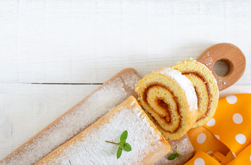 Delicious biscuit roll with apricot jam and powdered sugar on a white wooden table. Dessert for breakfast. Top view. Copy space