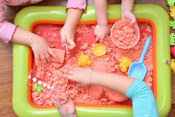 Children play with pink kinetic sand for sculpting figures. Top view, hands close up