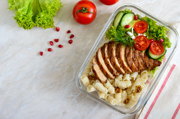 Lunch box: rotini with baked chicken breast and salad. Top view, flat lay. Delicious healthy lunch. The concept of healthy eating.