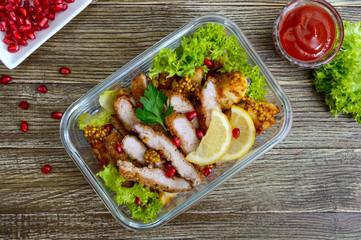Warm salad of baked potatoes, meat, greens with spicy sauce in a glass bowl on a wooden table. Lunch box. Top view.