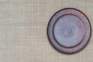 Round clay shallow brown plate on a light brown background. Copy space