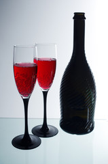 Two glasses of red champagne and a dark bottle on a light background.