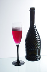 A glass of red champagne and a dark bottle on a light background.