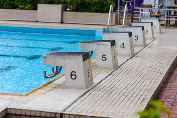 empty diving block stands with numbers in outdoor swimming pool on rainy day