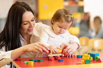 Kid with mother play with colorful wooden block toys on table in nursery