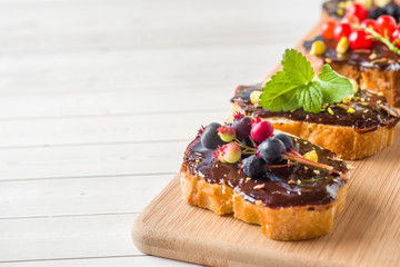 Sandwiches with chocolate paste, pistachio nuts and fresh berries on a wooden serving Board. Copy space