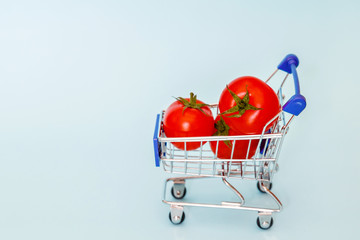 Grocery cart with cherry tomatoes standing on blue background. Place for text