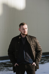 A man with a beard in a warm winter brown jacket poses for advertising of men's clothing in the winter. Advertising of men's clothing