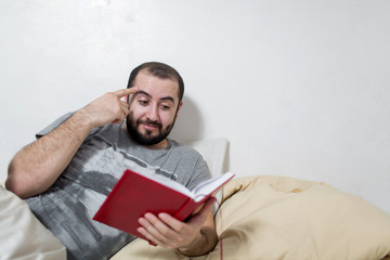 Young man pensive reads a book in the bedroom. White background.