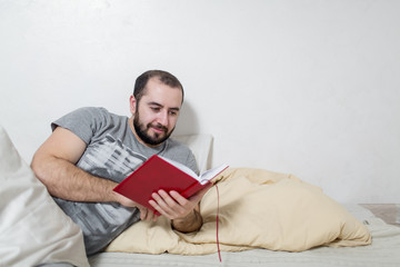 Fototapeta premium Young smiling man reading book in bedroom. White background.