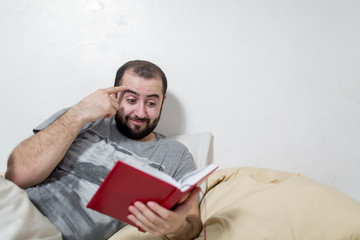 Young man pensive reads a book in the bedroom. White background.