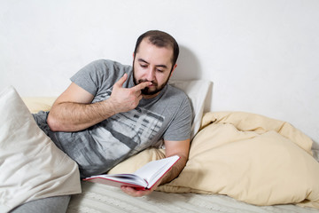 Young man pensive reads a book in the bedroom. White background.