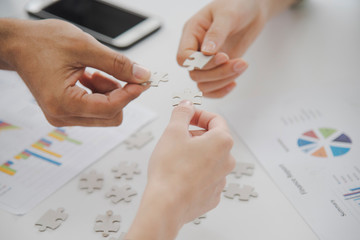Close up three Hands of business people holding jigsaw puzzle which paper document in background,...