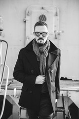 A man in a coat with a scarf poses on the street to advertise men's clothing. Black and white photo. Advertising menswear