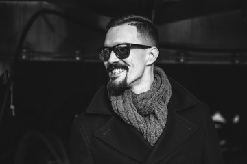 Obraz premium A man in a coat with a scarf poses on the street to advertise men's clothing. Black and white photo. Advertising menswear