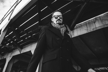 A man in a coat with a scarf poses on the street to advertise men's clothing. Black and white photo. Advertising menswear