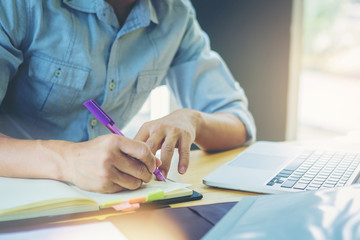 Businessman write a short note on opened notebook with pen and working with computer laptop.