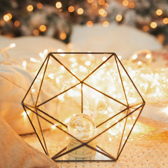 Glass icosahedron with snow globe inside near christmas tree with lights. Abstract geometric shape of glass.