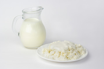  Milk jug and cottage cheese on a saucer. Isolated on white.