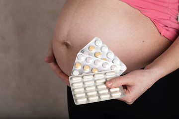 Obraz premium Young pregnant woman keeps films of pills close to her belly.