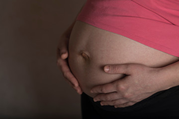Young pregnant woman touches her belly. Dramatic light.