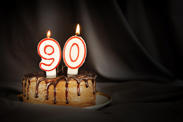 Ninety years anniversary. Birthday chocolate cake with white burning candles in the form of number...