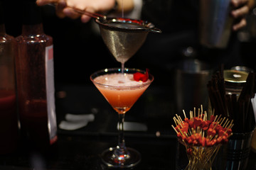 Bartender pouring tasty liquid into orange color cocktail at bar counter in nightclub bar