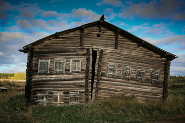 Obraz premium Front view of wooden log house in Russian village on a sunny day against bright cloudy sky and autumn background scenery, house cracked apart.